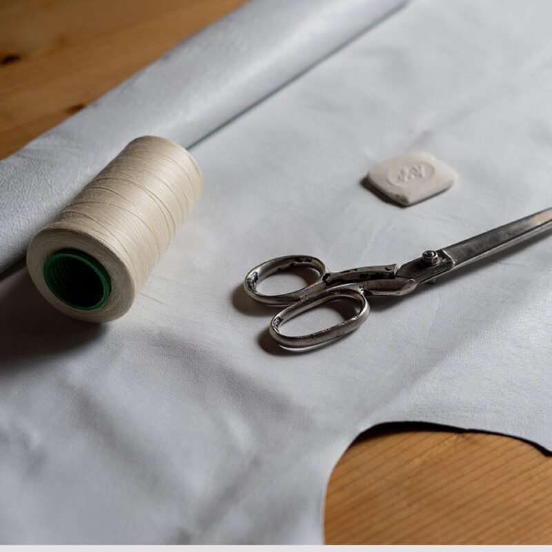 Natural gray leather for tailoring, threads and scissors on the table. Close up
